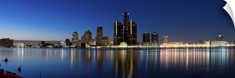 Narrow canvas print of the Detroit skyline illuminated in the evening with it's lights reflecting back on the water.