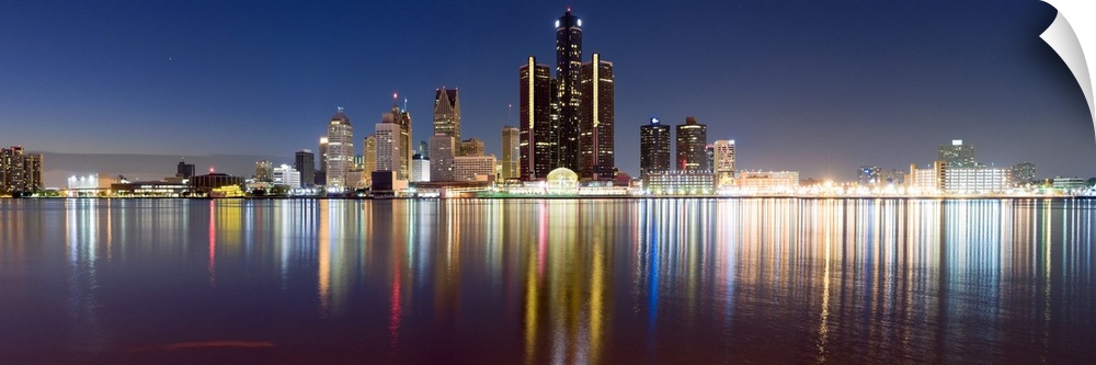 Wide angle photograph of the distant Detroit skyline, lit at night and reflecting in the waters of the Detroit River.