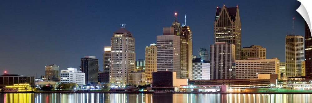 Nighttime panoramic shot of downtown Detroit buildings lit up at night and their light reflections in the Detroit River.