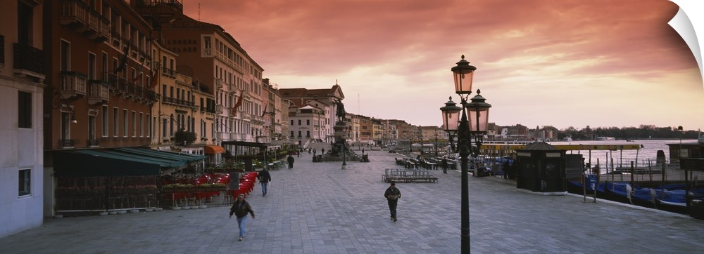 Panoramic photo of people walking on the promenade along the waterfront at sunrise in Venice, Italy.