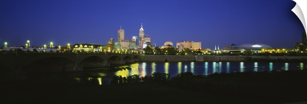 Big panoramic photo on canvas of a lit up city skyline past a bridge over a river.