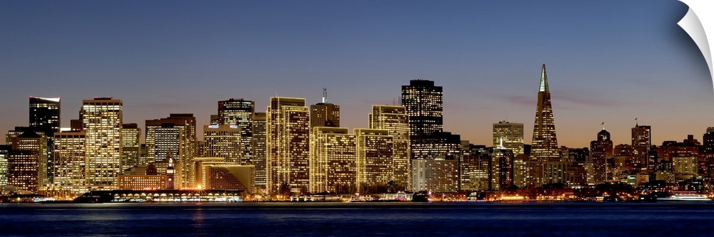Panoramic photograph of the San Francisco skyline with all of the buildings lit up under a sky at dusk.