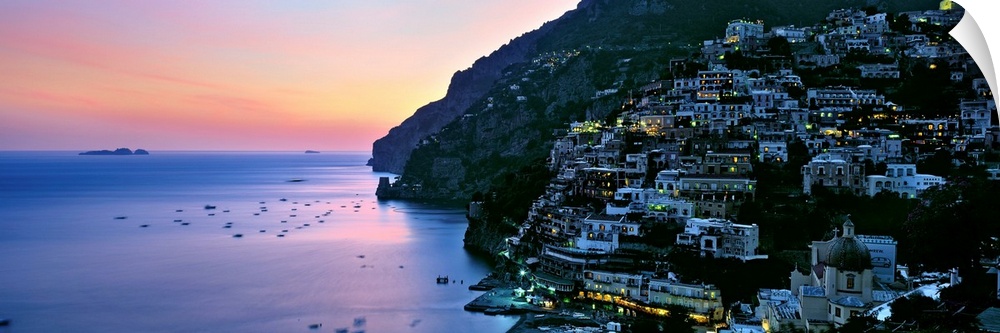 Rustic seaside village densely build up on a cliff side overlooking a harbor reflecting the setting sun.