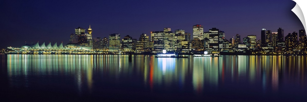 The Vancouver skyline is illuminated under a night sky and the lights reflecting in the water.
