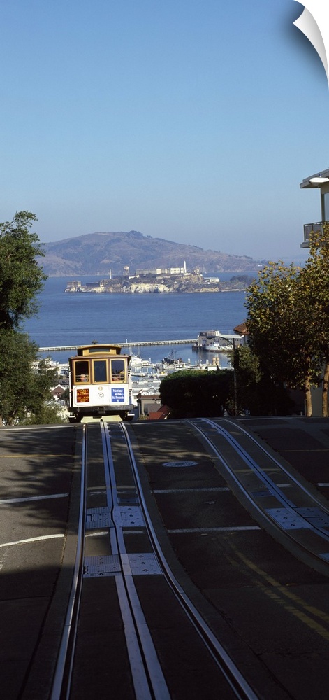 Vertical panoramic photograph of street trolley moving toward the horizon with harbor, waterfront, and mountains in the di...