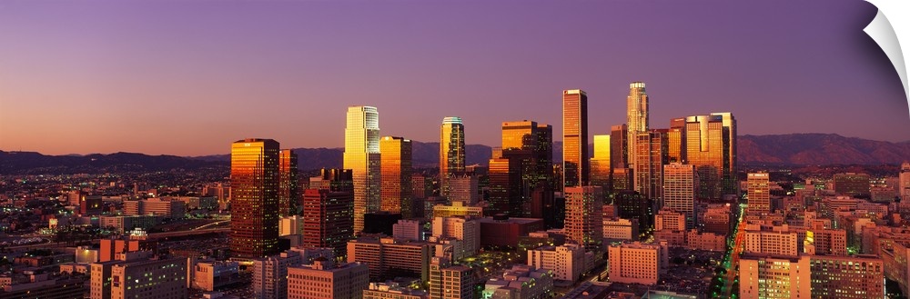 Panoramic photograph of west coast city skyline at dusk.  The buildings and skyscrapers are lit up with a long mountain ra...