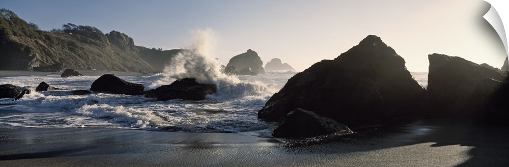 Panoramic photograph of shoreline with huge boulders with ocean waves and spray.