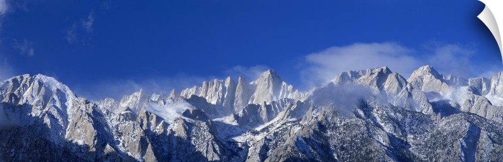 Panoramic photograph of snow covered Mount Whitney beneath a vibrant blue sky in California.