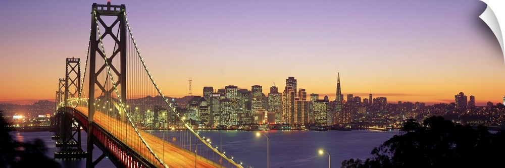 Twilight and the Golden Gate Bridge with the San Francisco Skyline with a purple and gold sky.