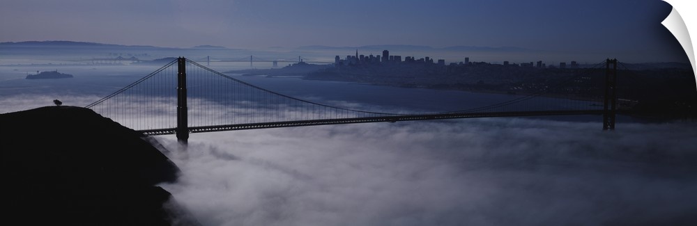 Large panoramic piece of the Golden Gate bridge that has dense fog just under it covering the water below.