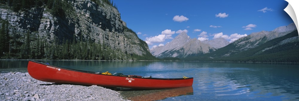 A long canoe is pictured in wide angle view as it sits half in half out of the water. Mountainous terrain lines the side a...