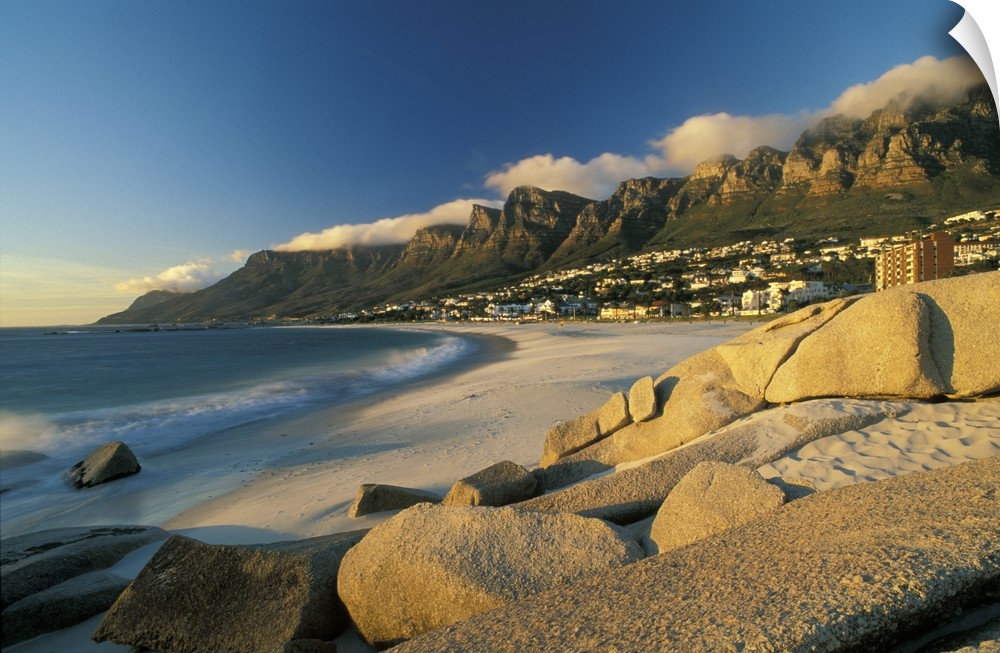 Horizontal, large photograph of rocks on a beach in front of Cape town, South Africa and mountains on the horizon.