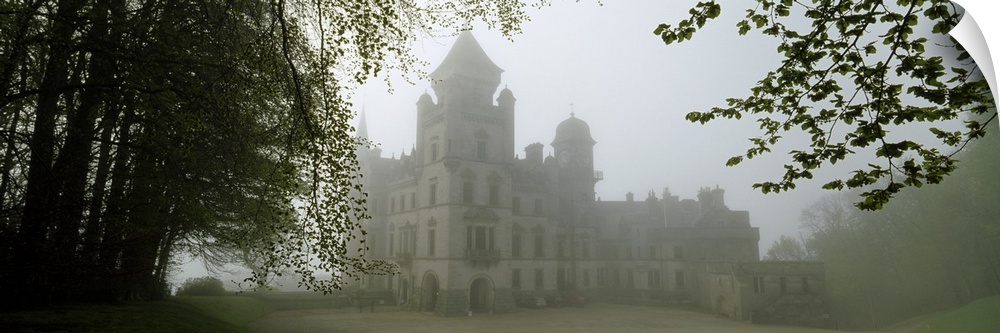 A large castle is faintly shown behind fog and surrounded by trees.