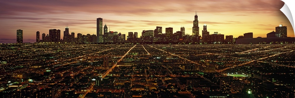 Panoramic photograph of skyline and city lit up at sunset.