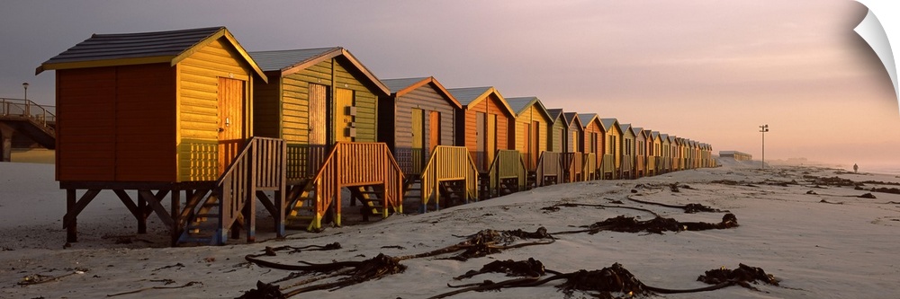 A panoramic photograph of a row of buildings built on the sandy shoreline glowing in the light of sunset.
