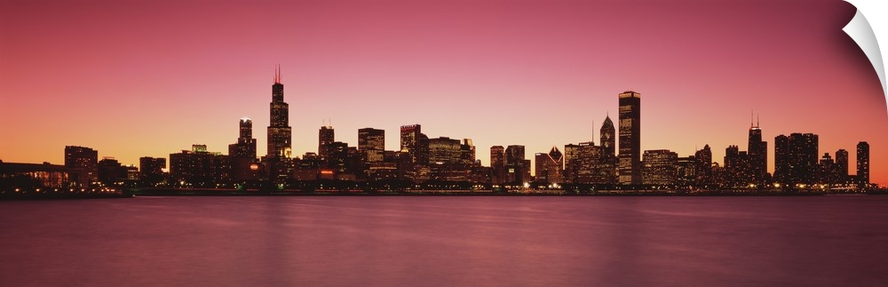 Panoramic photograph of lit up skyline and waterfront at dusk.