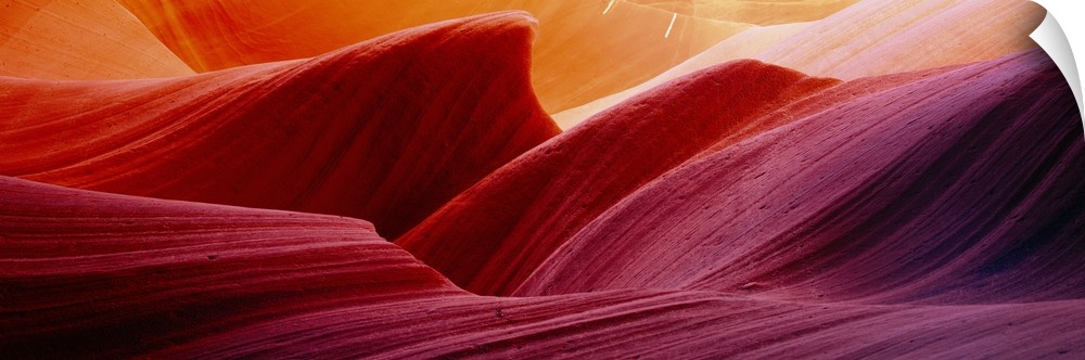 Panoramic photograph of eroded rock in Antelope Canyon, with light forming wavy patters as it bounces of the striations.