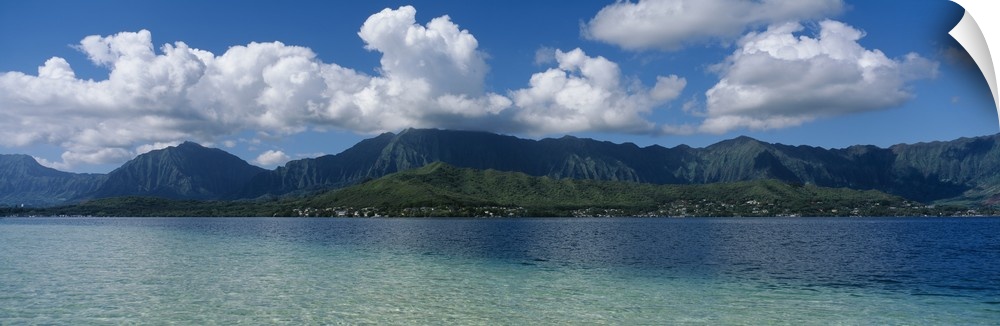 Panoramic photograph taken across the ocean looking at a Hawaiian island with immense clouds floating over.