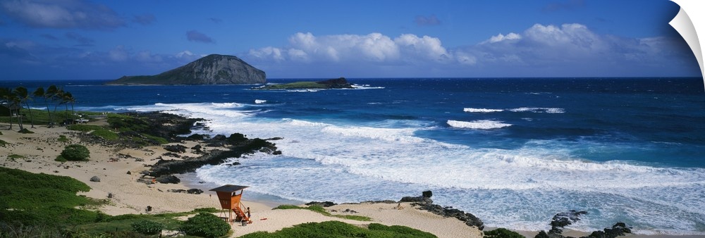 Waves crashing on the Makapuu Beach in Hawaii with an orange lifeguard tower look out over the water and palm trees blowin...