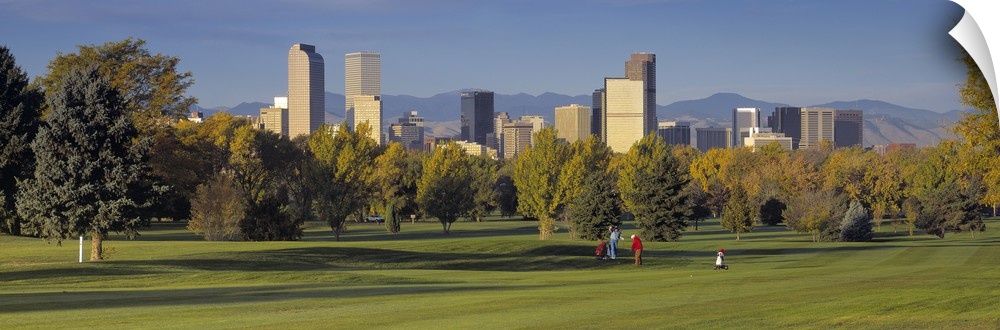 Big, panoramic photograph on the green of a golf course in Colorado, full of trees, the buildings of the Denver skyline in...