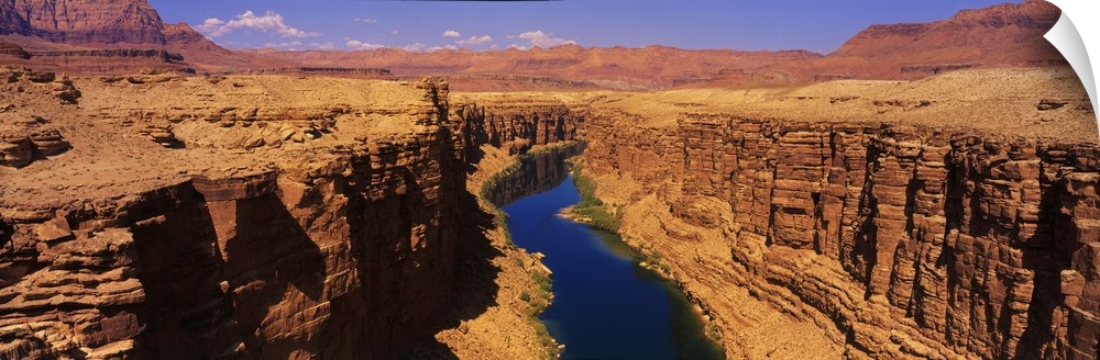 A panoramic photograph of an ancient waterway passing through the rock cliffs it has eroded over the millennia in the desert.