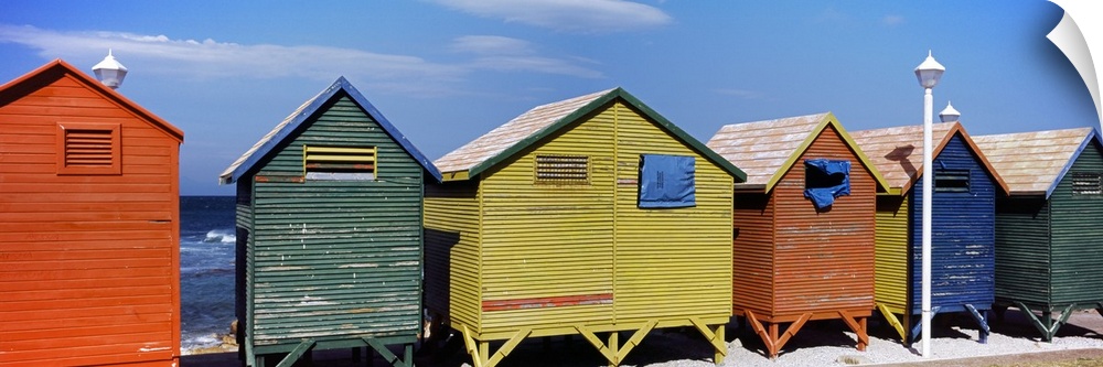 Panoramic photograph taken of multi-colored huts that line the beach with the ocean viewed in the distance.