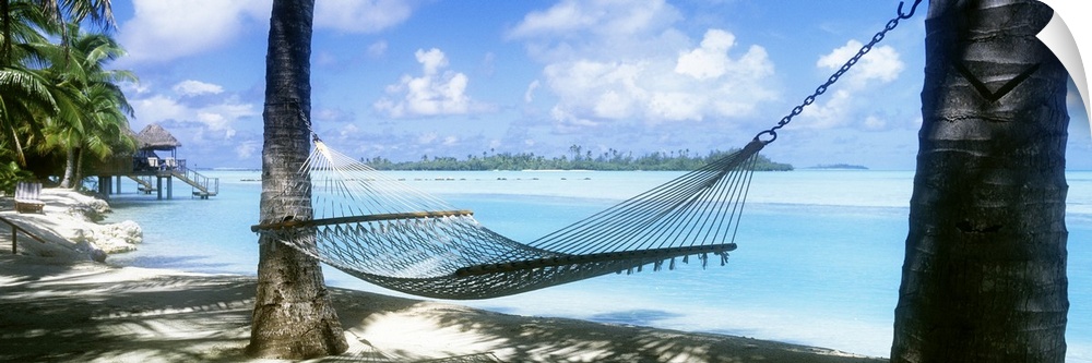 Panoramic photograph of a hammock hanging between two palm along the shore of the Cook Islands, clear blue waters of the S...