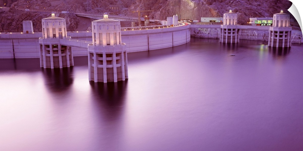 Horizontal photograph of the still surface of an impounded lake at twilight next to a concrete arch-gravity dam.