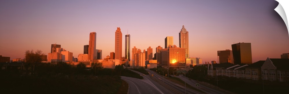 Giant, horizontal photograph of the sun rising over the Atlanta skyline, several roads and a row of buildings can be seen ...