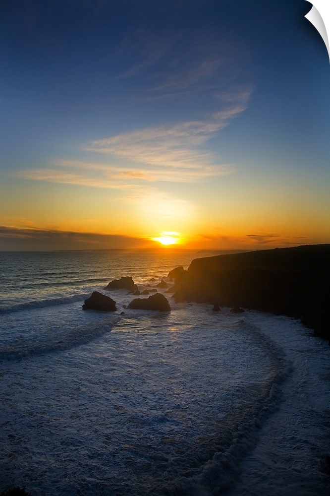 The sun is setting in the distance over the ocean with a large cliff to the right that is silhouetted.