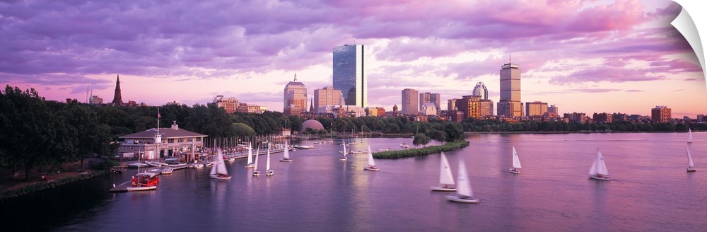 Panoramic photograph of skyline and waterfront at sunset.  There are sailboats in the water under a cloudy sky.