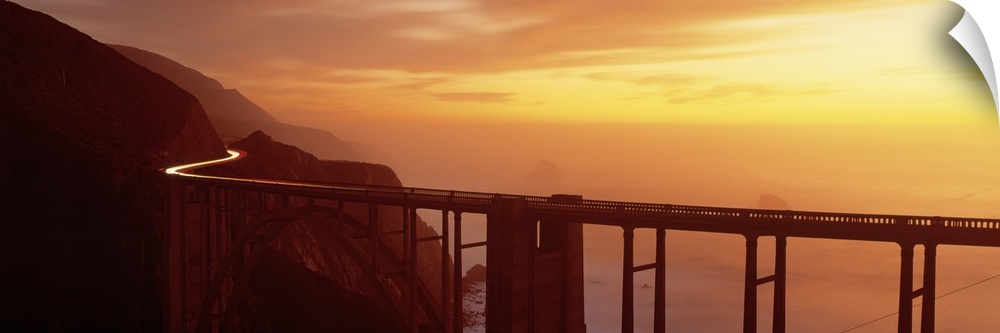 Panoramic photograph of overpass winding through mountains over the ocean at sunset.