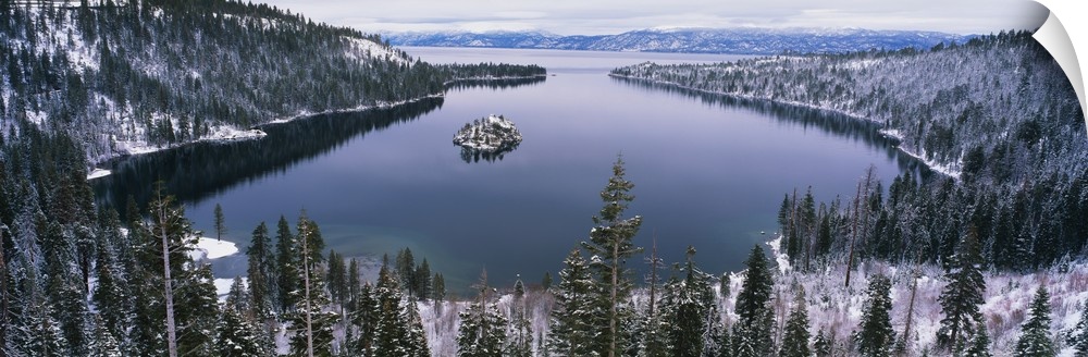 Panoramic photograph of inlet surrounded by snow covered forest under a cloudy sky.