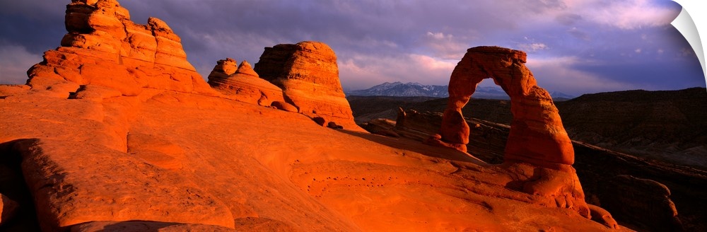A landscape photograph that is a panoramic shot of a wind eroded rock face illuminated a sunset.