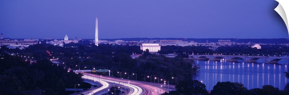 Wide angle view of the nations capital during dusk with the monuments lit up and the highway illuminated with cars lights.