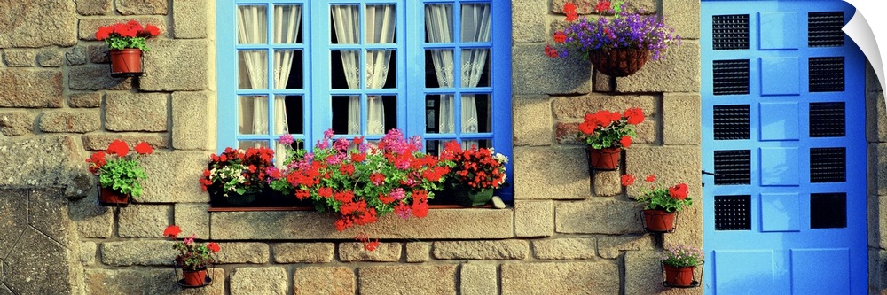 Blue door and window sit in the stone faoade of brick French house with planters full of red flowers.