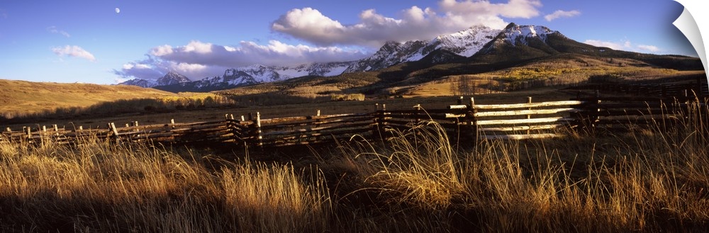 A large panoramic picture of Colorado mountains with a fence and tall grass in the foreground.