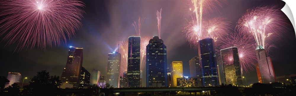Giant photograph at nighttime displays vibrant pyrotechnics bursting above a set of large skyscrapers located within the l...