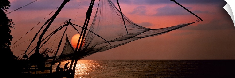 Panoramic photo of fishing nets silhouetted against a big setting sun.