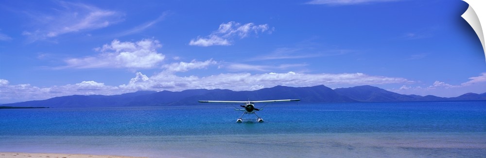 Private propeller plane floating on the water near the shoreline with low mountains and cloudy skies overhead.