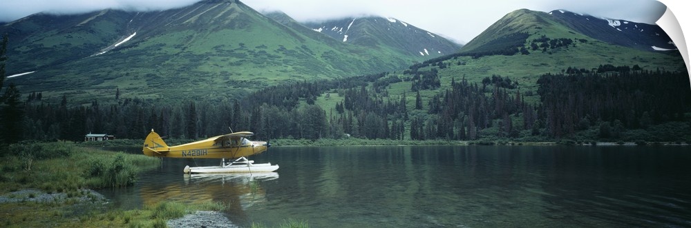 Panoramic photograph of airplane on skis in lake with mountains in the distance.