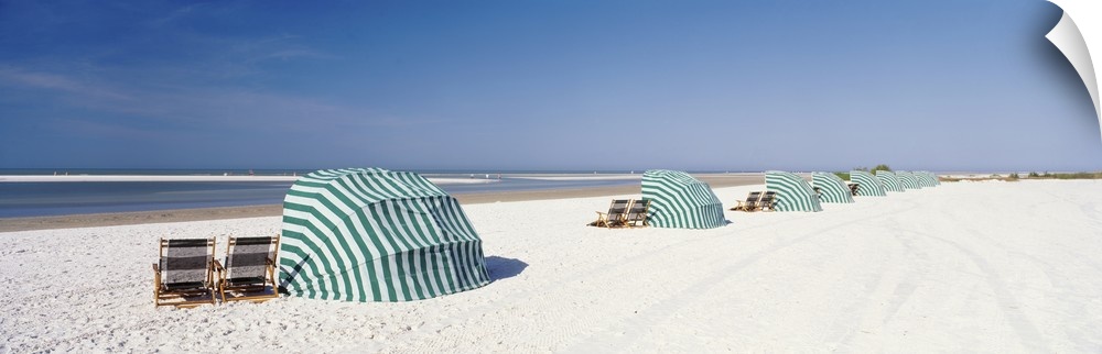 Panoramic photograph of shoreline wish beach chairs and umbrellas under a clear sky.
