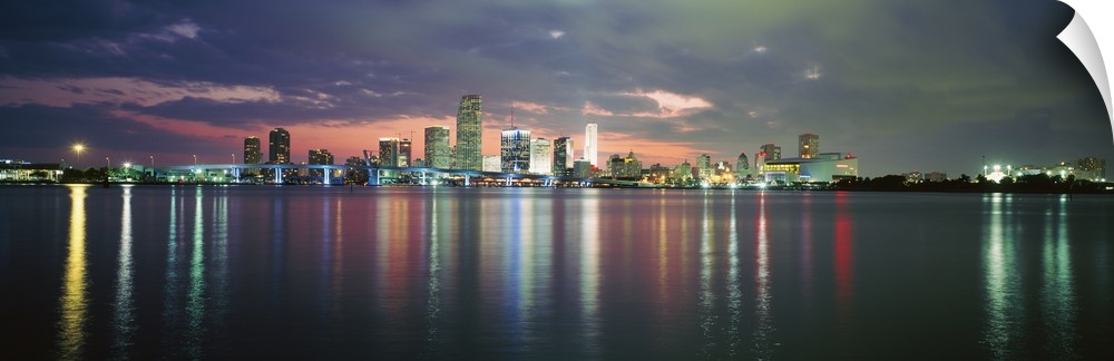 This city scape photograph shows the city from a distance reflecting on the water on panoramic shaped wall art.