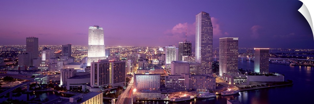 Aerial  photograph taken of an illuminated Miami skyline underneath a dusk sky.