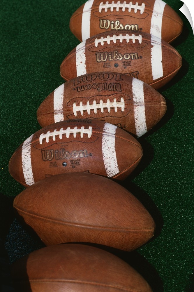 Photograph of six footballs lined up in a row on a field.