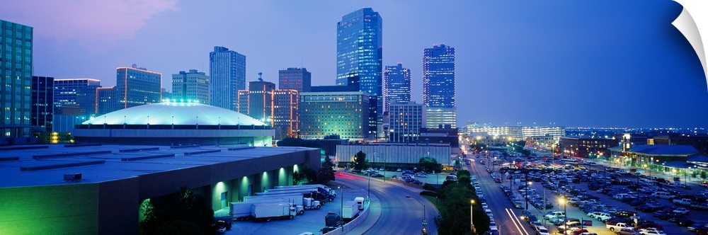 The city of Fort Worth is illuminated under a dusk sky with the buildings mostly shown to the left of this panoramic piece.