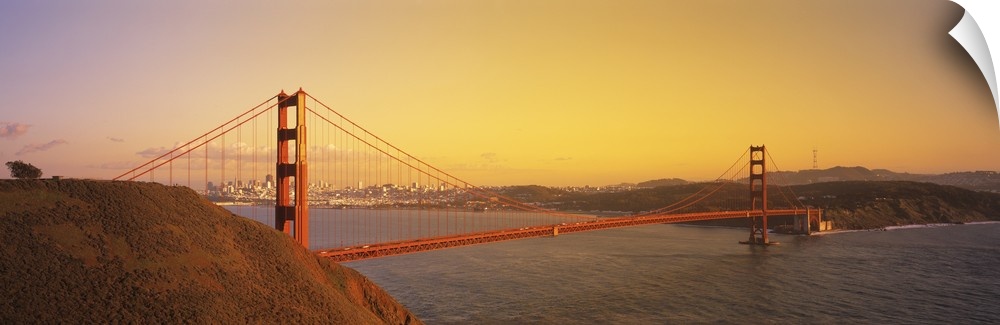 Panoramic photo of the Golden Gate Bridge with a bright sky and the city in the distance.