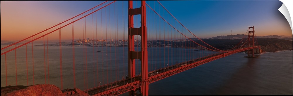 Panoramic photograph of the iconic suspension bridge in California's Bay Area during sunset, with the city in the distance.