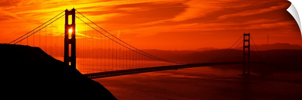 This oversized wall art is a panorama of San Francisco Bay at sunset where the suspension bridge is a dark silhouette in t...