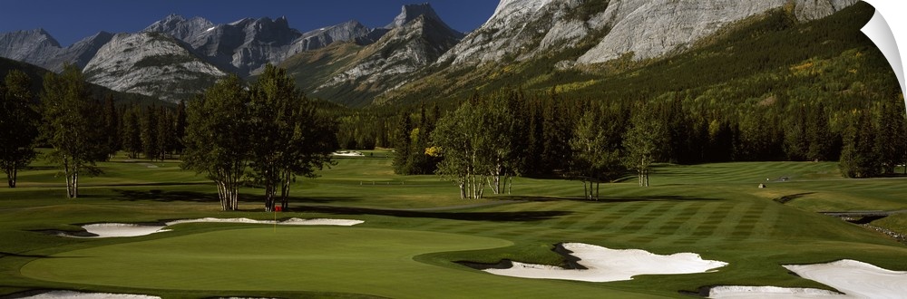 Panoramic photograph taken on a golf course of one of the holes that is surrounded by a mountain view.